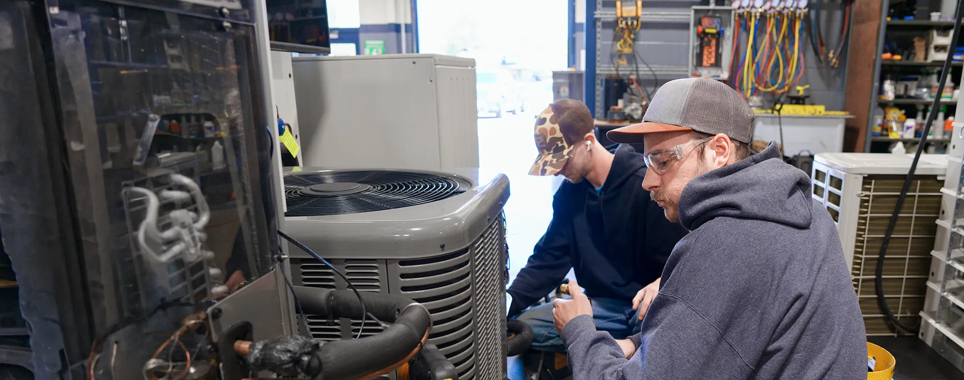 Two students working on an HVAC training unit surrounded by air conditioning equipment in a lab.