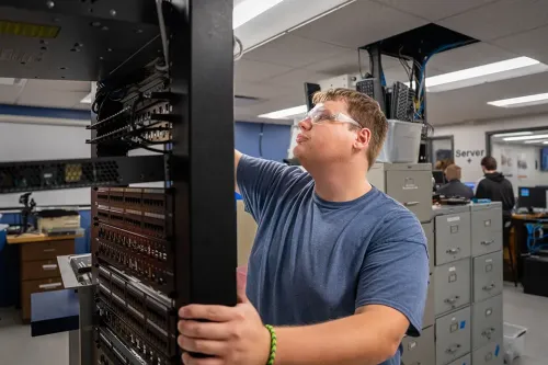 Person wearing safety glasses installing or inspecting network equipment in a server rack.