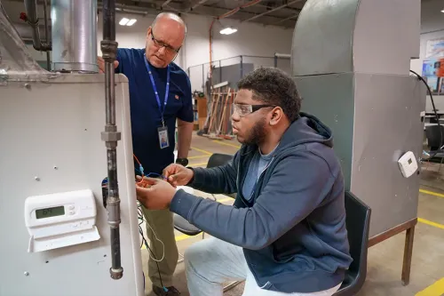 Student wiring an HVAC system while an instructor observes in a training lab.