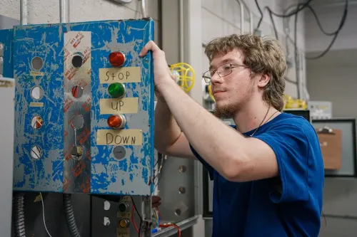 Student working on a blue industrial control panel with labeled buttons reading STOP, UP, and DOWN.